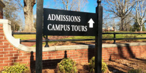 A signboard outside college, that reads, 'Admissions, campus tours' with an upward arrow next to it