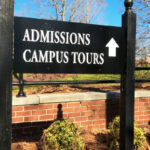 A signboard outside college, that reads, 'Admissions, campus tours' with an upward arrow next to it