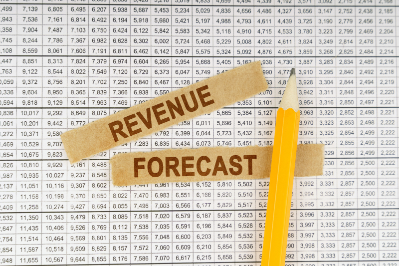 In this image, there is a document with reports of revenue forecasts and a yellow pencil placed on top of the document.
